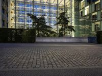 the clock is displayed in front of some tall buildings behind a tree lined street with shrubs