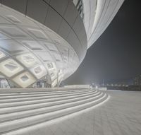 a night time photograph shows steps leading up to an enormous building with lit up windows and large round ceilings