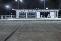 a deserted parking lot lit up by street lamps at night with one man walking by the bench