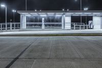 a deserted parking lot lit up by street lamps at night with one man walking by the bench