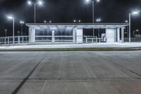 a deserted parking lot lit up by street lamps at night with one man walking by the bench