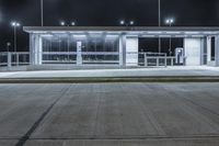 a deserted parking lot lit up by street lamps at night with one man walking by the bench