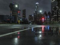 the traffic light reflects on a wet street at night as cars go by on the sidewalk