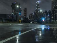the traffic light reflects on a wet street at night as cars go by on the sidewalk