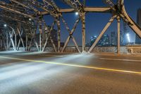 an empty street under a lit up bridge in the night sky of an urban area