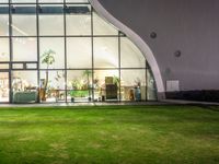 a green area with large windows, grass and plants at night in front of it