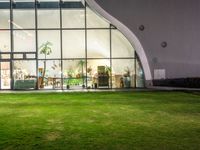 a green area with large windows, grass and plants at night in front of it