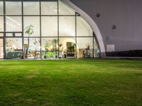 a green area with large windows, grass and plants at night in front of it