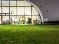 a green area with large windows, grass and plants at night in front of it