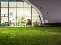 a green area with large windows, grass and plants at night in front of it