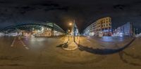 a photo of some street with buildings and a person crossing it at night near a bus stop