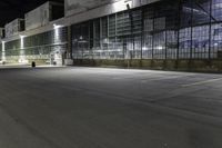 empty parking lot at night in front of large glass building at the corner of the street