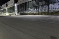 empty parking lot at night in front of large glass building at the corner of the street