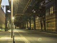 a man walking across an empty street at night underneath a bridge above the city lights