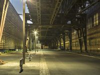 a man walking across an empty street at night underneath a bridge above the city lights