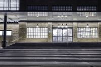 the front of a building lit up at night with stairs going to the door and a clock in the front