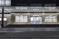 the front of a building lit up at night with stairs going to the door and a clock in the front