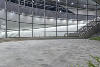 a sidewalk near many windows and stairs in an office building in the night with no people