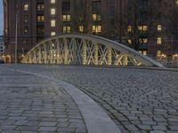 an arch bridge across the street at night near buildings in a city street with people walking and a lamp post