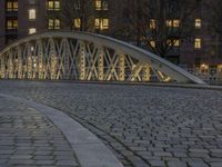 an arch bridge across the street at night near buildings in a city street with people walking and a lamp post