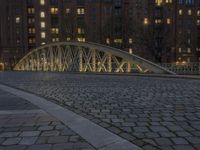 an arch bridge across the street at night near buildings in a city street with people walking and a lamp post