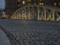 an arch bridge across the street at night near buildings in a city street with people walking and a lamp post