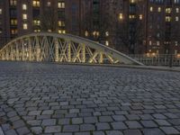 an arch bridge across the street at night near buildings in a city street with people walking and a lamp post