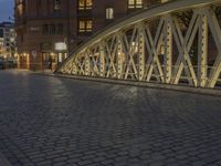 an arch bridge across the street at night near buildings in a city street with people walking and a lamp post