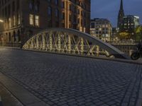 an arch bridge across the street at night near buildings in a city street with people walking and a lamp post