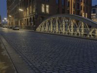 an arch bridge across the street at night near buildings in a city street with people walking and a lamp post