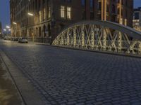 an arch bridge across the street at night near buildings in a city street with people walking and a lamp post