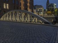 an arch bridge across the street at night near buildings in a city street with people walking and a lamp post