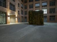 the large sculpture stands outside of a brick building by night in the dark lighted courtyard