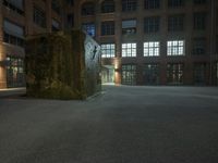 the large sculpture stands outside of a brick building by night in the dark lighted courtyard