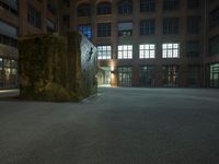 the large sculpture stands outside of a brick building by night in the dark lighted courtyard