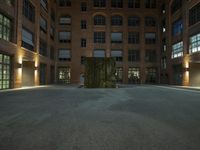 the large sculpture stands outside of a brick building by night in the dark lighted courtyard