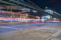 light trails through a street with many buildings in the background and cars travelling under an overhead bridge