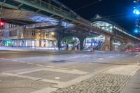 light trails through a street with many buildings in the background and cars travelling under an overhead bridge