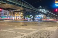 light trails through a street with many buildings in the background and cars travelling under an overhead bridge