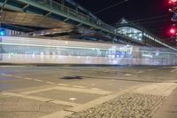 light trails through a street with many buildings in the background and cars travelling under an overhead bridge