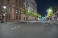 street light in night time with street view of buildings and cars driving on road and trees lining street