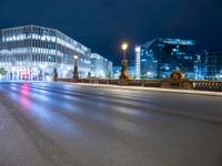 the empty city street is seen at night with lights from several buildings on either side