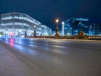 the empty city street is seen at night with lights from several buildings on either side