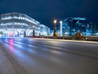 the empty city street is seen at night with lights from several buildings on either side