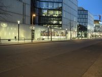 a paved street in the middle of buildings with tall windows at night, with car lights on