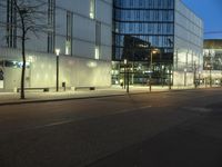 a paved street in the middle of buildings with tall windows at night, with car lights on