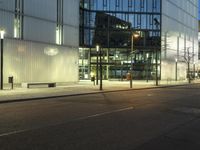 a paved street in the middle of buildings with tall windows at night, with car lights on