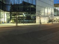 a paved street in the middle of buildings with tall windows at night, with car lights on