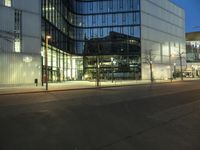 a paved street in the middle of buildings with tall windows at night, with car lights on