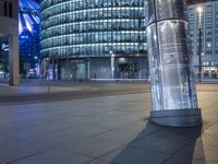 an empty city street at night as a cyclist passes by a tall building lit up in blue light